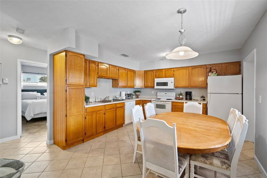 A kitchen features oak cabinets, white appliances, a dining table, and light-colored tile flooring — 380 BASE AVENUE E UNIT 202, VENICE, FL