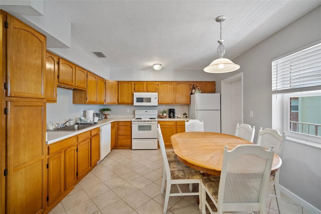 A kitchen with oak cabinets, white appliances, tile flooring, and a dining table — 380 BASE AVENUE E UNIT 202, VENICE, FL
