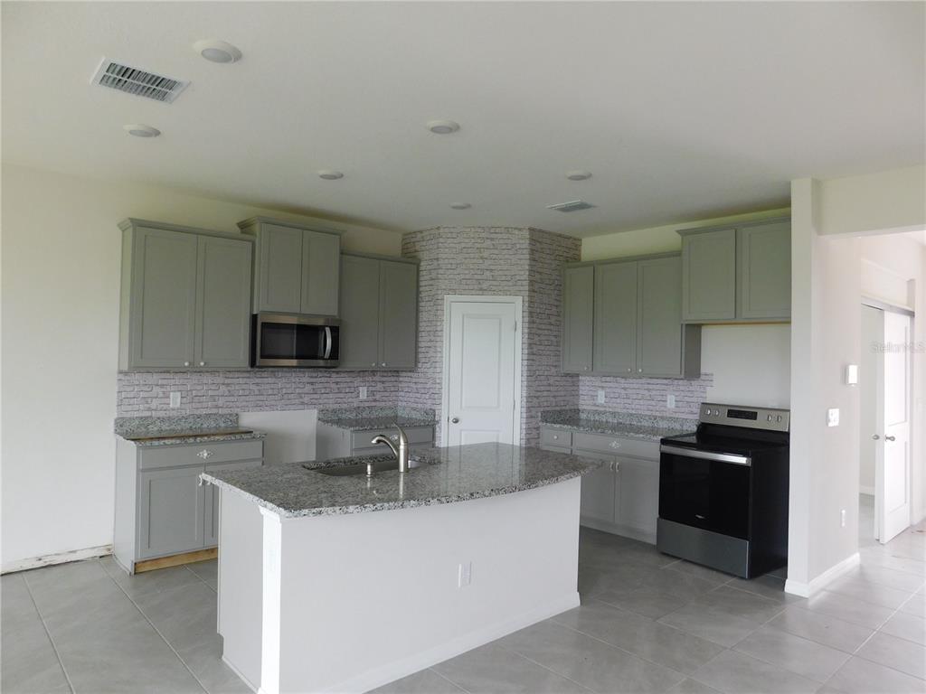 A kitchen features gray cabinets, granite countertops, a center island, and a faux-brick backsplash — 3813 LIVELY CORAL PLACE, BRADENTON, FL