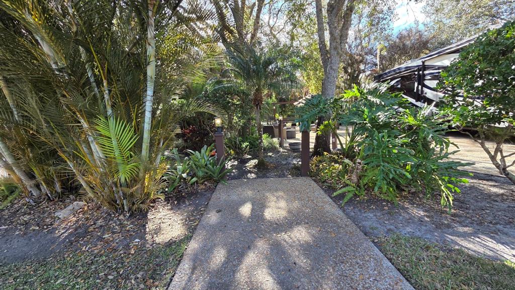 A concrete walkway leads through a landscaped garden toward a patio area and parked RV — 359 POSSUM PATH, RIVER RANCH, FL