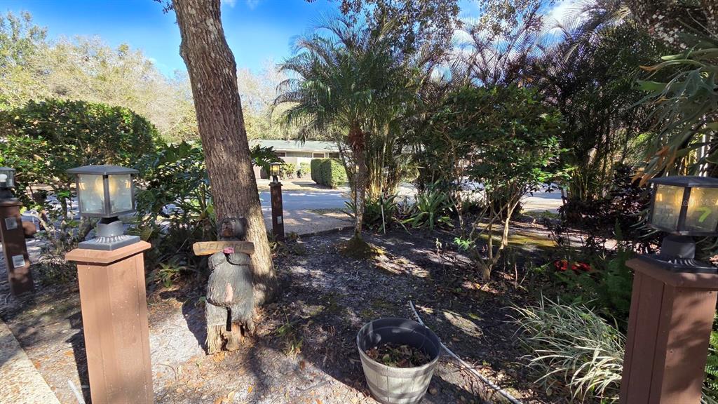 A wooden bear statue holding a welcome sign stands in a landscaped front yard — 359 POSSUM PATH, RIVER RANCH, FL