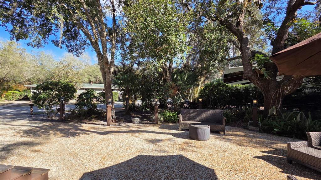 A patio with a gravel surface, outdoor furniture, and mature trees in a wooded setting — 359 POSSUM PATH, RIVER RANCH, FL