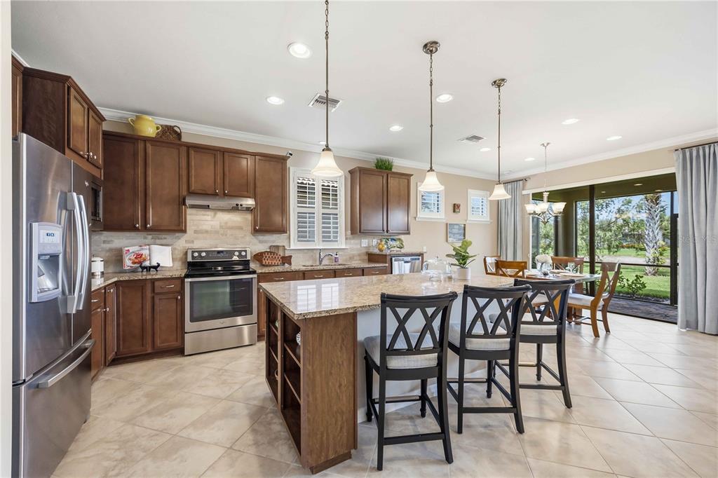 A kitchen features dark wood cabinets, granite countertops, a center island, and stainless steel appliances — 19731 QUISTO STREET, VENICE, FL