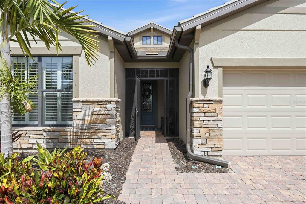 A stone-accented house exterior features a paved walkway leading to a screened front entryway — 19731 QUISTO STREET, VENICE, FL