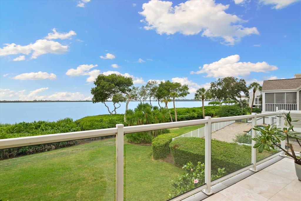 A balcony with a glass railing overlooks a grassy lawn, lush landscaping, and a large lake — 76 TIDY ISLAND BOULEVARD, BRADENTON, FL