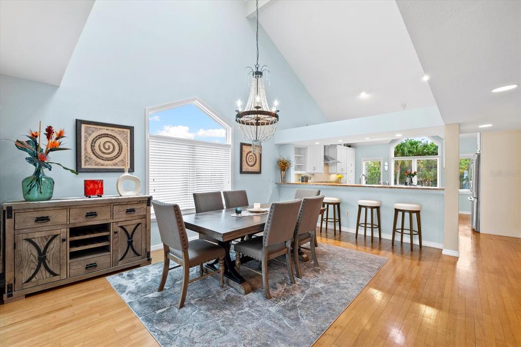 A dining area with a vaulted ceiling, chandelier, wooden table, and an adjacent kitchen breakfast bar — 76 TIDY ISLAND BOULEVARD, BRADENTON, FL