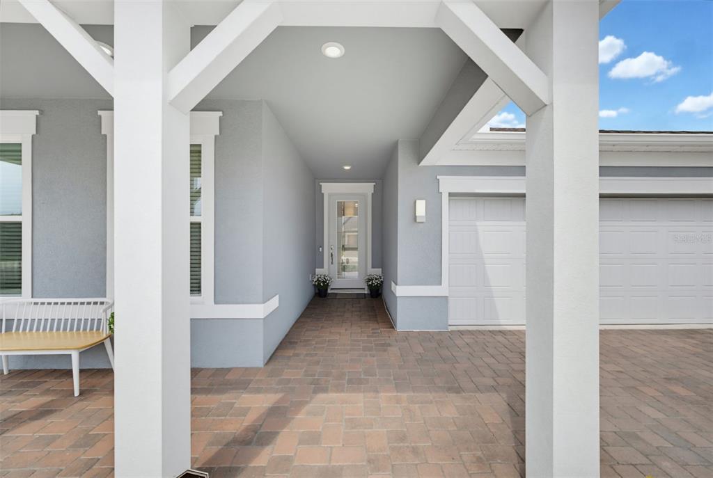 A covered entryway features a paver floor, white support columns, and a glass-paneled front door — 6391 SHIMMERING SHORES LANE, ST CLOUD, FL