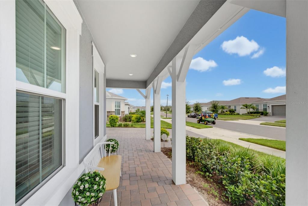 A covered front porch with a white bench overlooks a suburban street with a golf cart — 6391 SHIMMERING SHORES LANE, ST CLOUD, FL