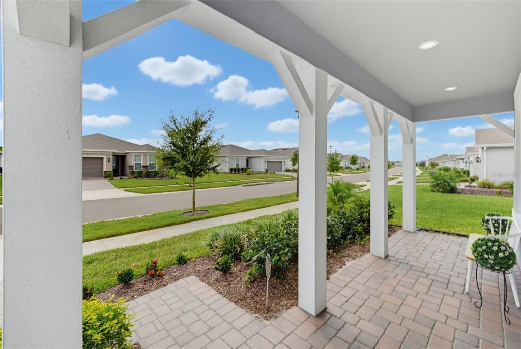 A covered front porch with paver flooring overlooks a suburban street with houses and lawns — 6391 SHIMMERING SHORES LANE, ST CLOUD, FL