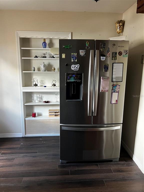 A stainless steel refrigerator stands next to a built-in white shelving unit on wood flooring — 1220 S BAY STREET S, EUSTIS, FL