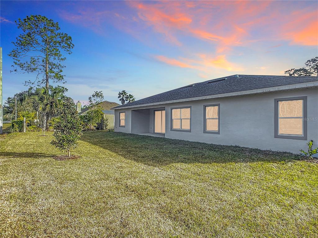 The exterior view shows the back of a gray house with a lawn at sunset — 16 EGAN DRIVE, PALM COAST, FL