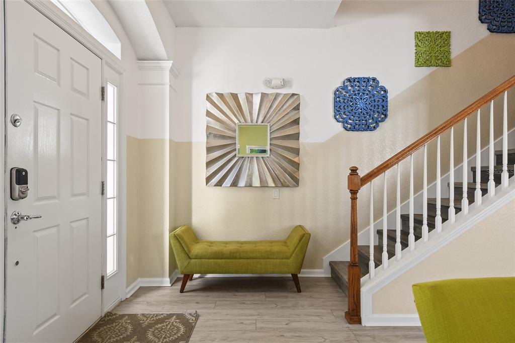 An entryway features a green bench, a sunburst mirror, wall art, and a wooden staircase — 2536 HOLTROCK STREET, KISSIMMEE, FL