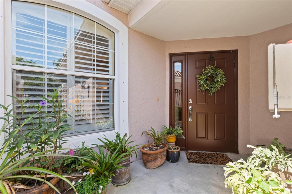 A front entryway features a brown door with a wreath, a large window, and potted plants — 2061 CARRIAGE LANE UNIT 104, CLEARWATER, FL