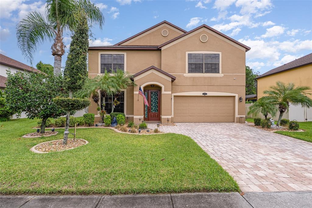A two-story tan stucco house features a brick-paved driveway, a front porch, and landscaping — 912 WHETSTONE PLACE, ROCKLEDGE, FL