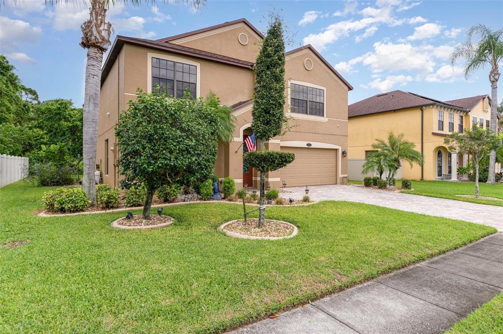 A two-story tan house with a paved driveway, a front lawn, and manicured landscaping — 912 WHETSTONE PLACE, ROCKLEDGE, FL