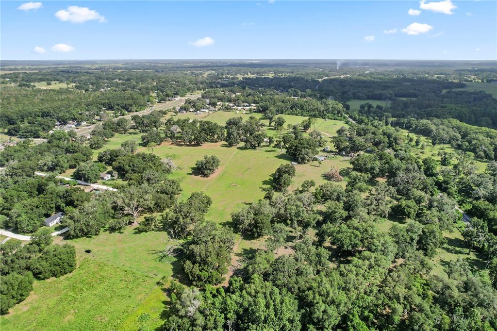 An aerial view shows a large, grassy pasture surrounded by dense trees and rural landscape — 37952 CRYSTAL WAY, DADE CITY, FL