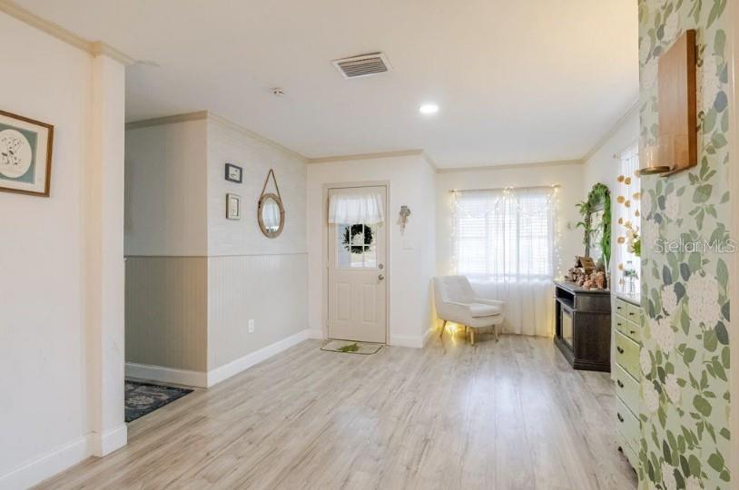 A bright room features light wood-look flooring, wainscoting, a front door, and floral wallpaper — 1225 KING AVENUE, LAKELAND, FL