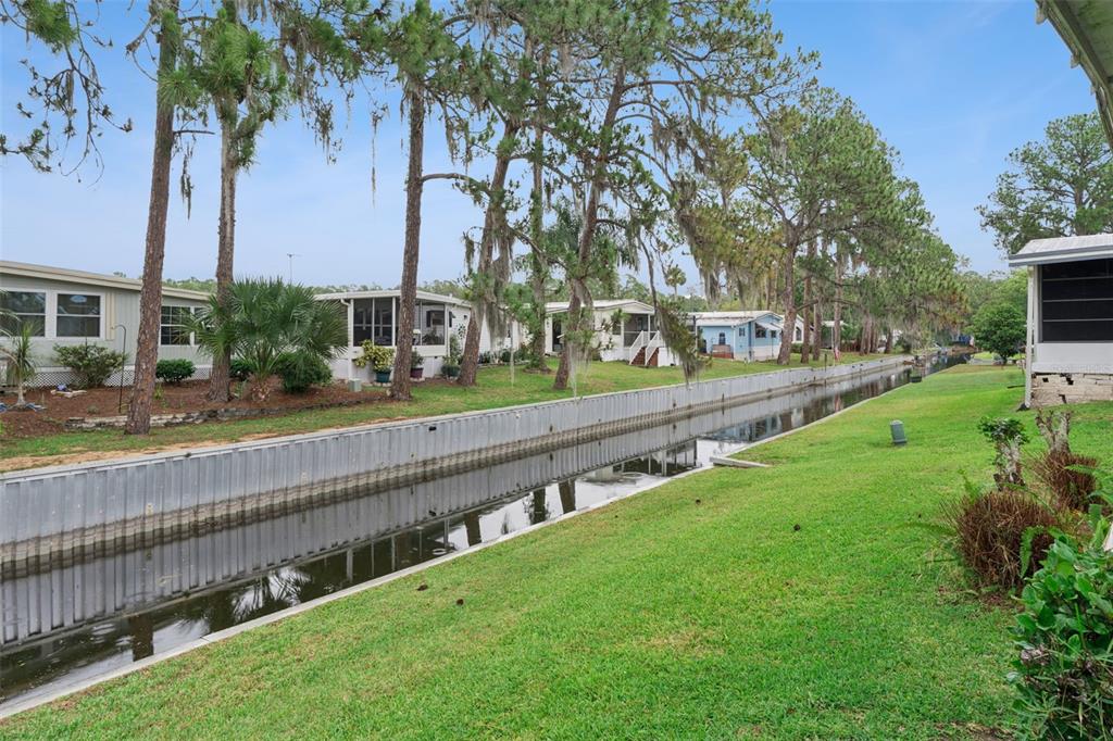 A canal runs between rows of manufactured homes lined with pine trees and green grass — 102 PARKLAND DRIVE, EUSTIS, FL