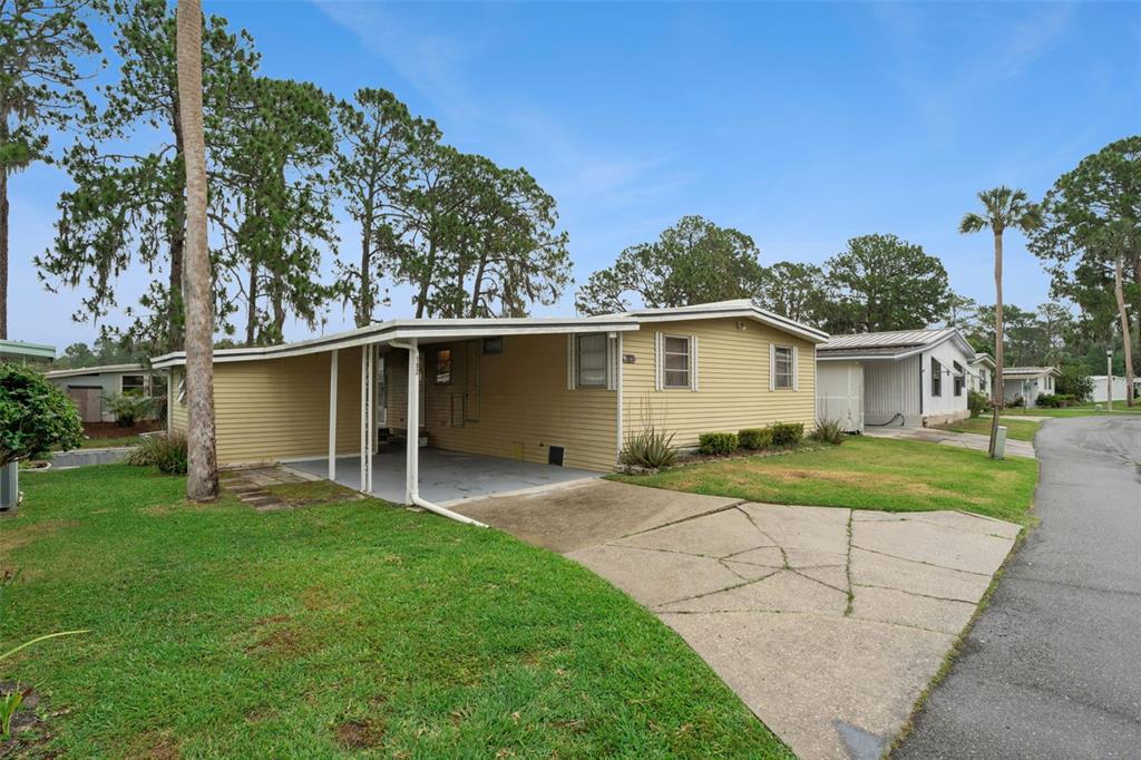 A single-story yellow mobile home with a carport and a cracked concrete driveway — 102 PARKLAND DRIVE, EUSTIS, FL