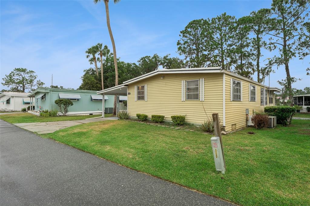 A yellow mobile home with a covered carport sits on a grassy lot — 102 PARKLAND DRIVE, EUSTIS, FL