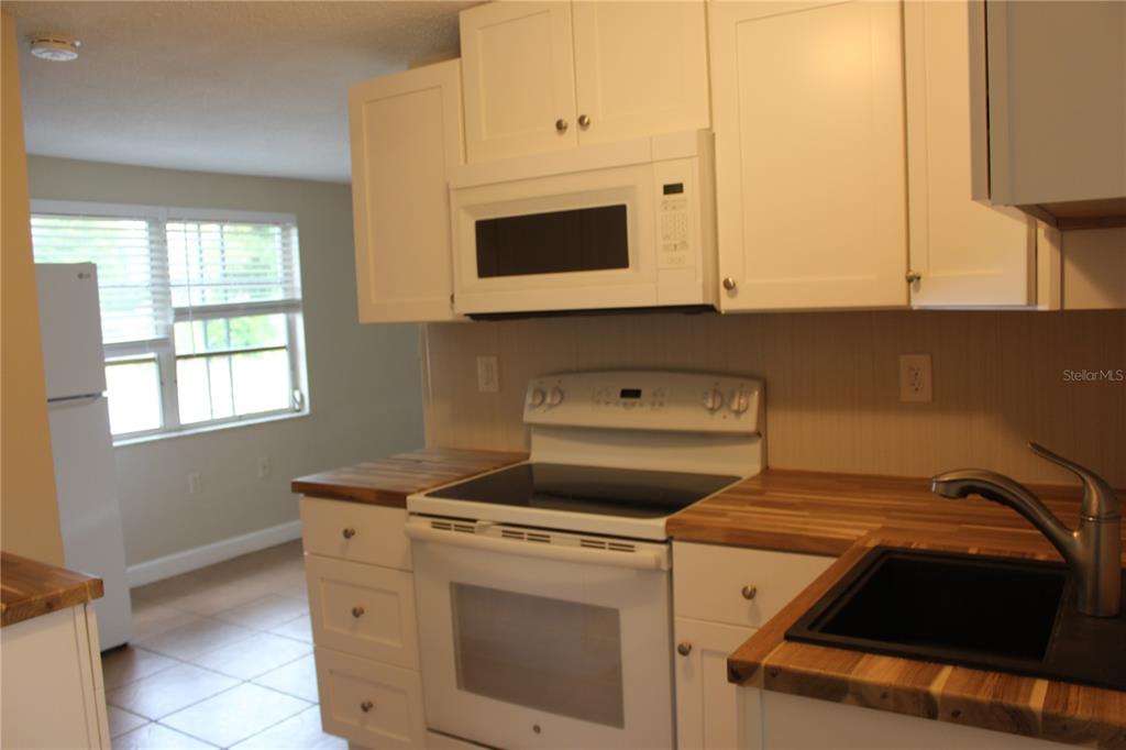 A kitchen features white cabinets, a white stove, a microwave, and wood-look countertops — 4424 TERRY LOOP UNIT A, NEW PORT RICHEY, FL