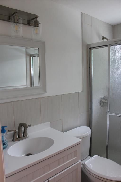 A bathroom features a white vanity, a mirror, a toilet, and a glass-enclosed shower — 4424 TERRY LOOP UNIT A, NEW PORT RICHEY, FL