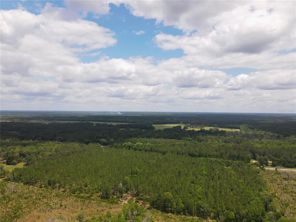 An aerial view shows a vast landscape of dense forest and open fields under a cloudy sky — TBD N STATE ROAD 121 UNIT 1, ALACHUA, FL