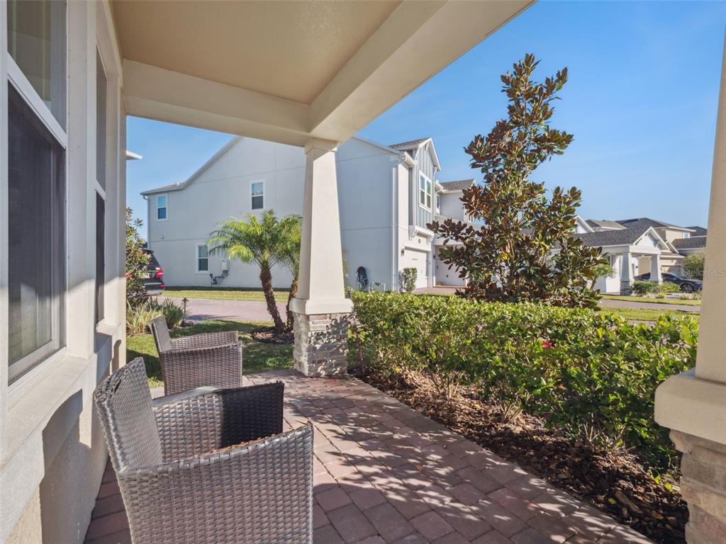 A covered front porch features brick pavers, two wicker chairs, and a view of neighborhood homes — 14345 WABASSO LOOP, WINTER GARDEN, FL
