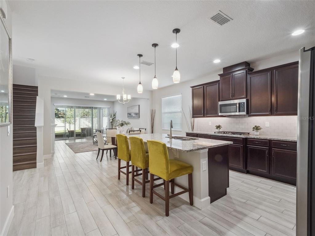A kitchen with dark wood cabinets, granite countertops, and yellow bar stools on light flooring — 14345 WABASSO LOOP, WINTER GARDEN, FL