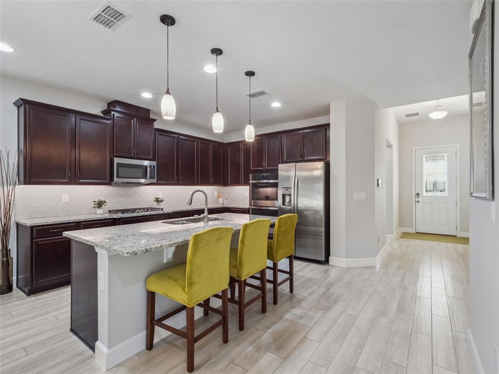 A kitchen features dark wood cabinets, granite countertops, a central island, and three yellow stools — 14345 WABASSO LOOP, WINTER GARDEN, FL