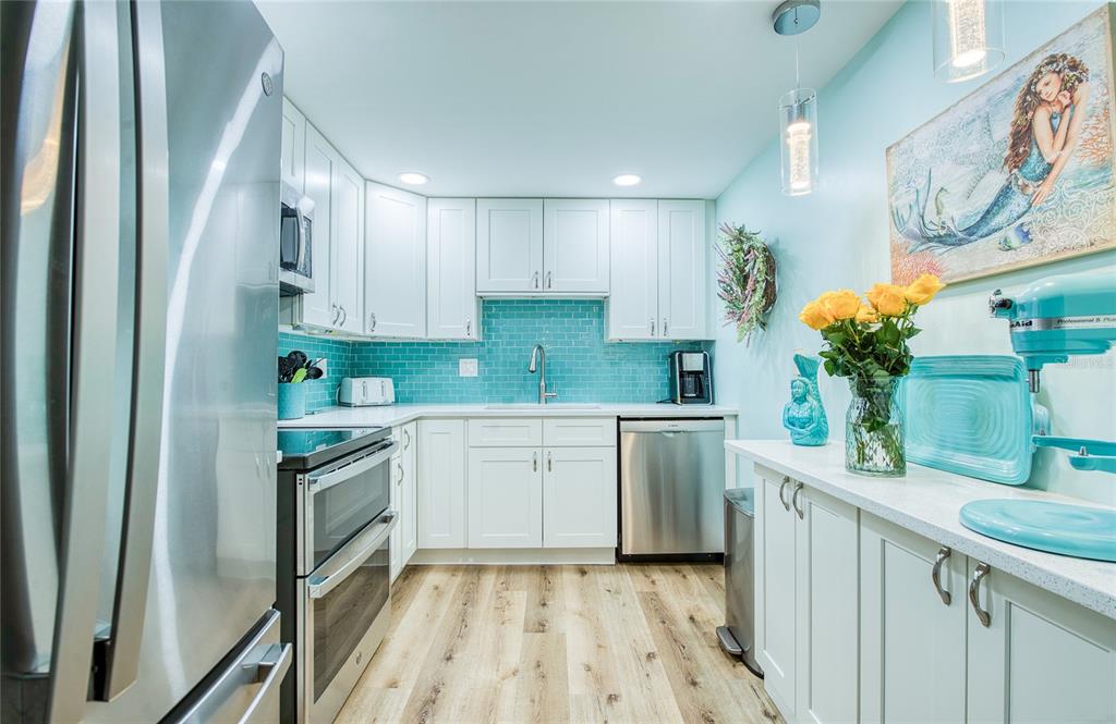 A kitchen features white cabinetry, a turquoise subway tile backsplash, and stainless steel appliances — 10216 REGAL DRIVE UNIT 310, LARGO, FL