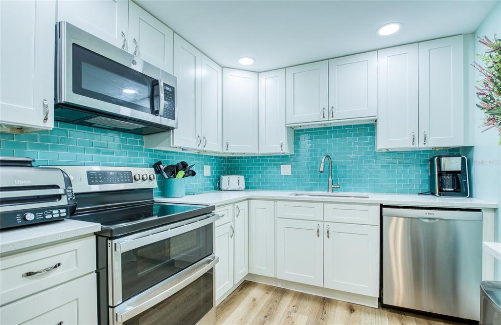 A kitchen features white cabinets, stainless steel appliances, and a bright teal subway tile backsplash — 10216 REGAL DRIVE UNIT 310, LARGO, FL