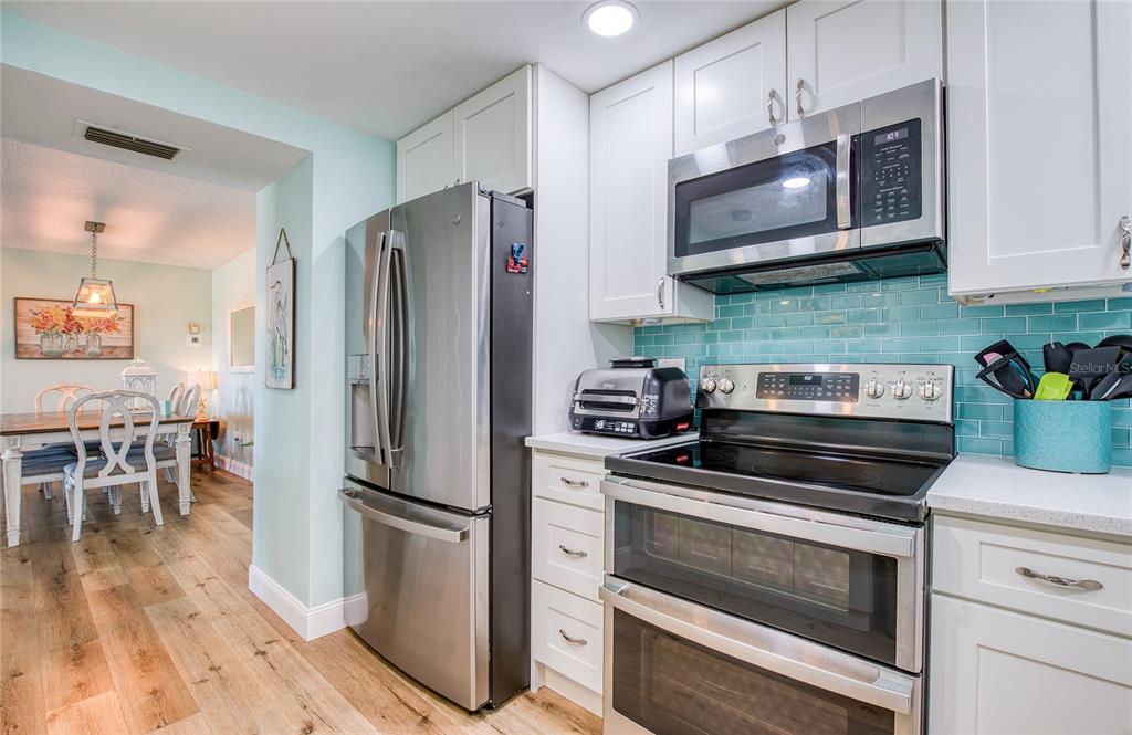 A kitchen features stainless steel appliances, white cabinets, and a teal subway tile backsplash — 10216 REGAL DRIVE UNIT 310, LARGO, FL