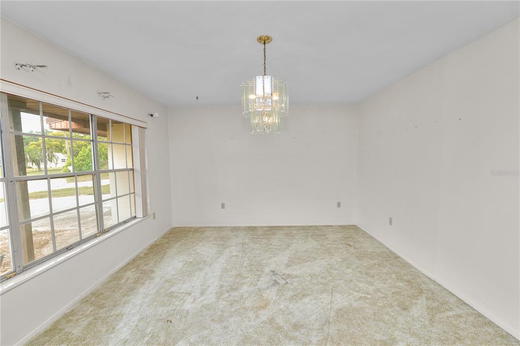 An empty room with beige carpet, white walls, a crystal chandelier, and a large window — 760 MANOR DRIVE, BARTOW, FL