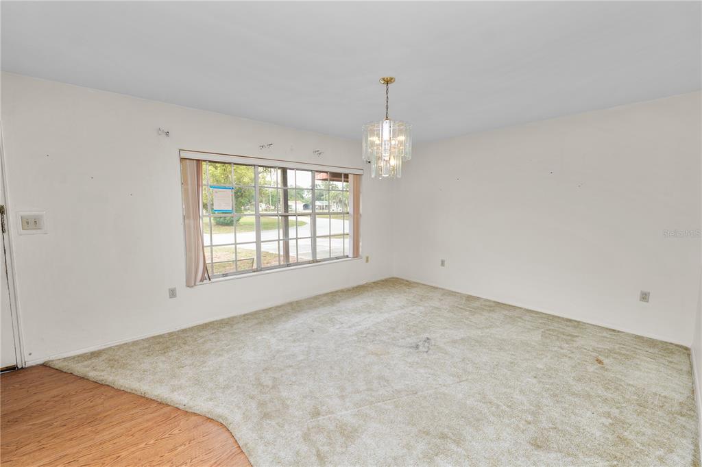 A room with beige wall-to-wall carpeting, white walls, a large window, and a crystal chandelier — 760 MANOR DRIVE, BARTOW, FL