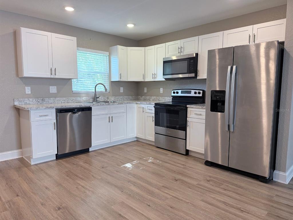 A kitchen features white cabinets, stainless steel appliances, and light wood-look flooring — 1139 SYCAMORE STREET, LAKELAND, FL