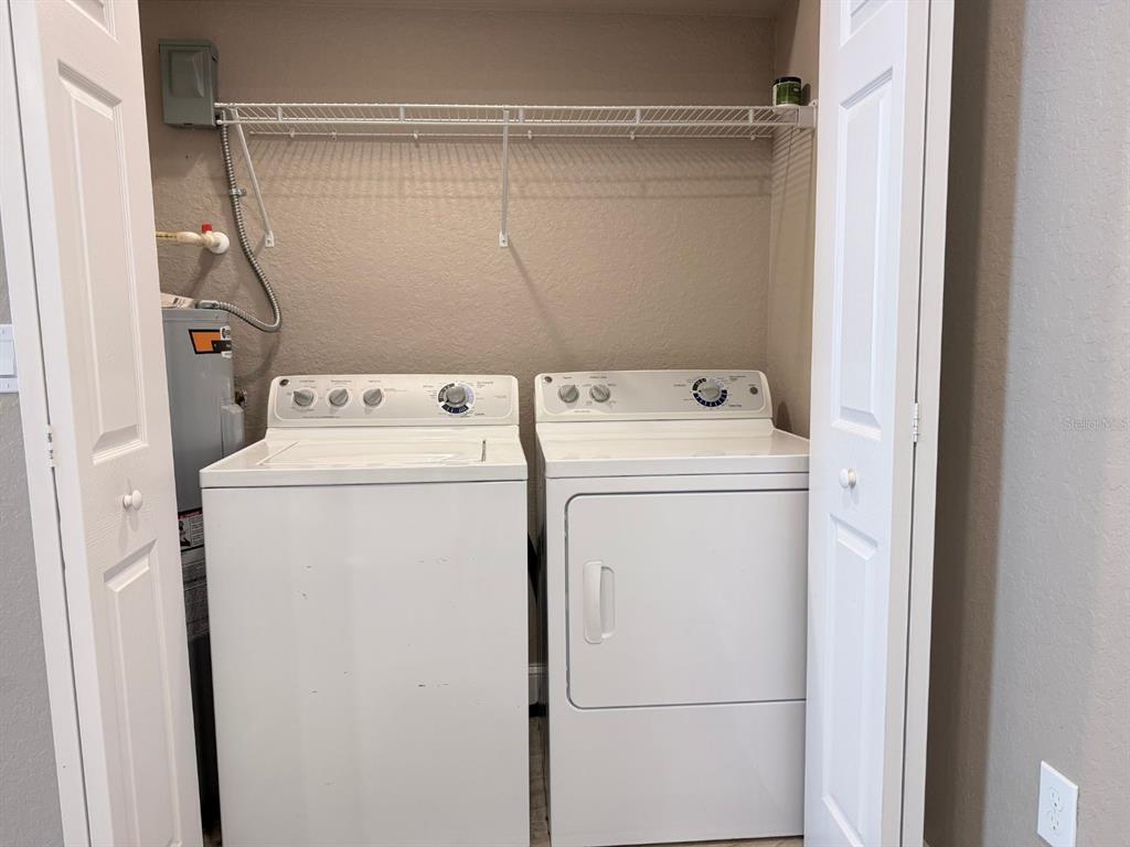 A laundry closet contains a white top-loading washer and dryer beneath a wire shelf — 1139 SYCAMORE STREET, LAKELAND, FL