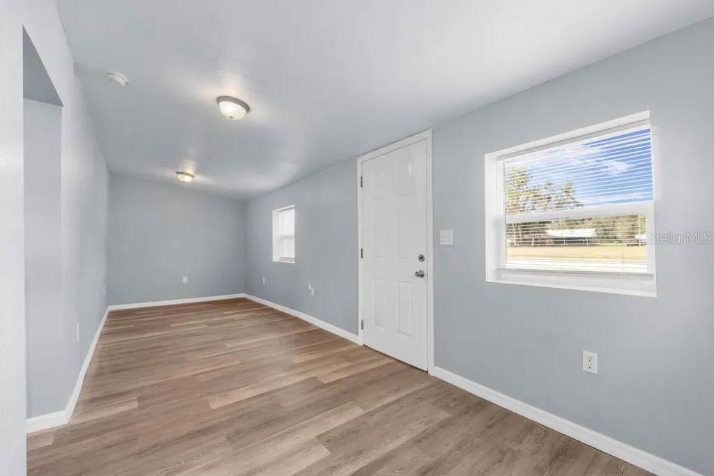 An empty room with light blue walls, wood-look flooring, a white door, and two windows — 515 S CHARLESTON AVENUE, FORT MEADE, FL