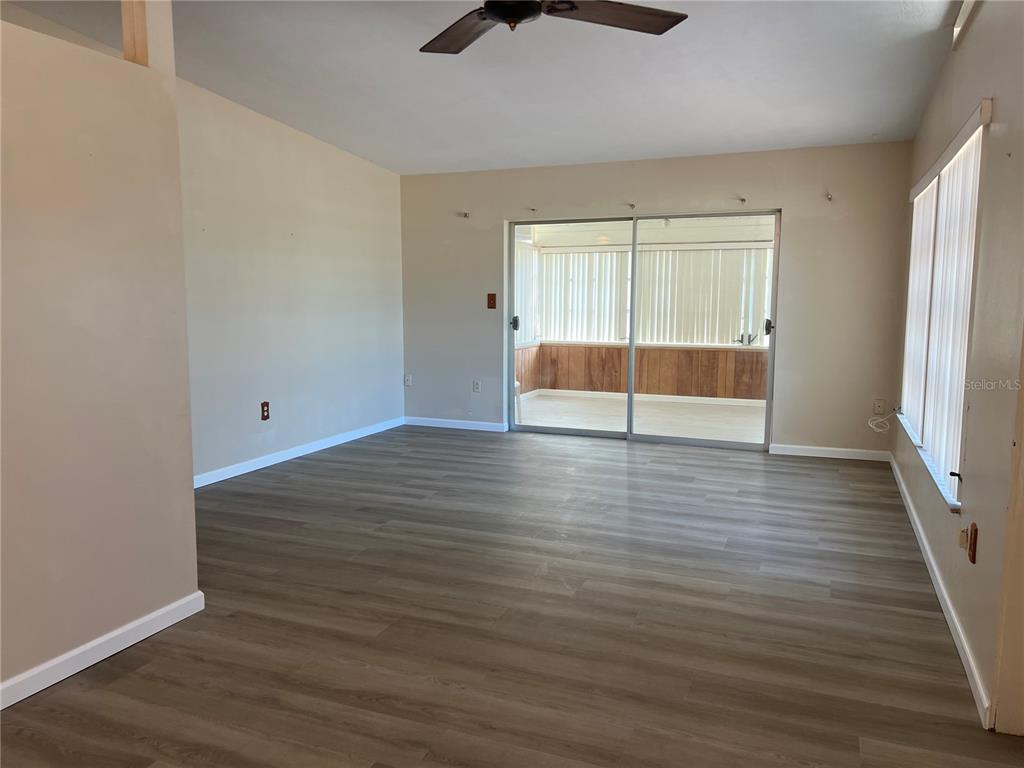 An empty living room features light-colored walls, wood-look flooring, a ceiling fan, and sliding doors — 321 ALBA STREET E, VENICE, FL