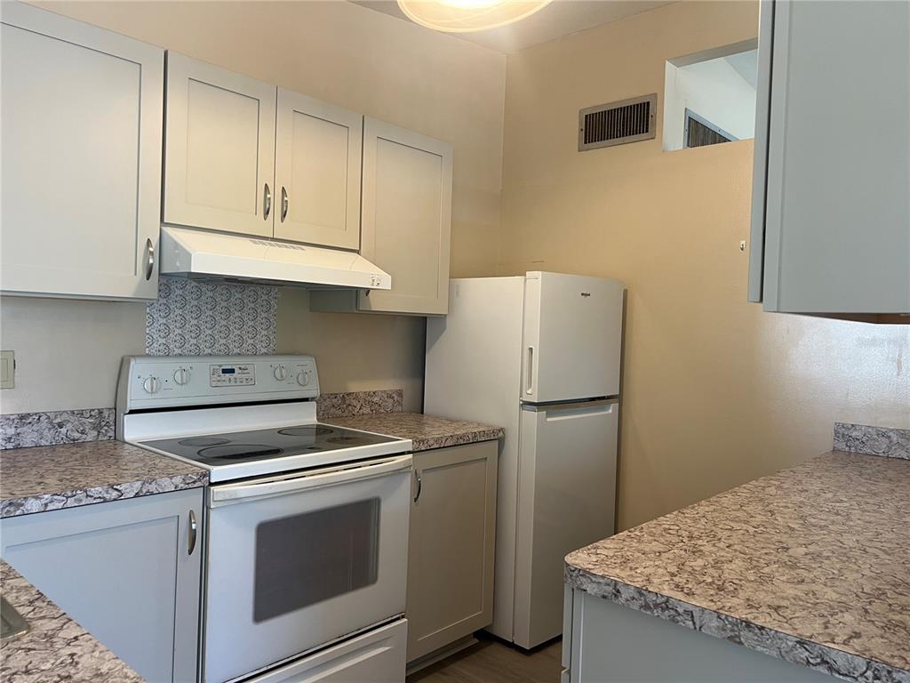 A kitchen features light gray cabinets, a white stove, a white refrigerator, and patterned countertops — 321 ALBA STREET E, VENICE, FL