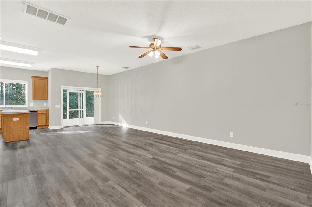 An open-concept living area features gray walls, wood-look flooring, a ceiling fan, and a kitchen — 17454 STINCHAR DRIVE, LAND O LAKES, FL