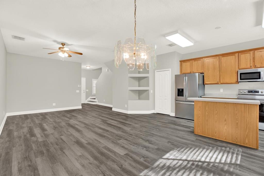 An open-concept kitchen and living area features wood-look flooring, light gray walls, and oak cabinetry — 17454 STINCHAR DRIVE, LAND O LAKES, FL