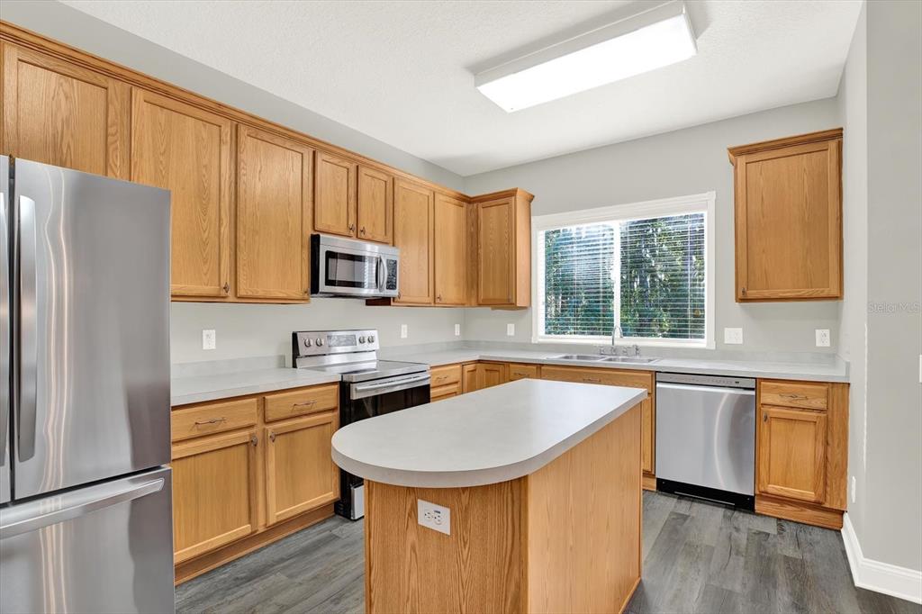 A kitchen features oak cabinets, stainless steel appliances, a center island, and gray laminate flooring — 17454 STINCHAR DRIVE, LAND O LAKES, FL