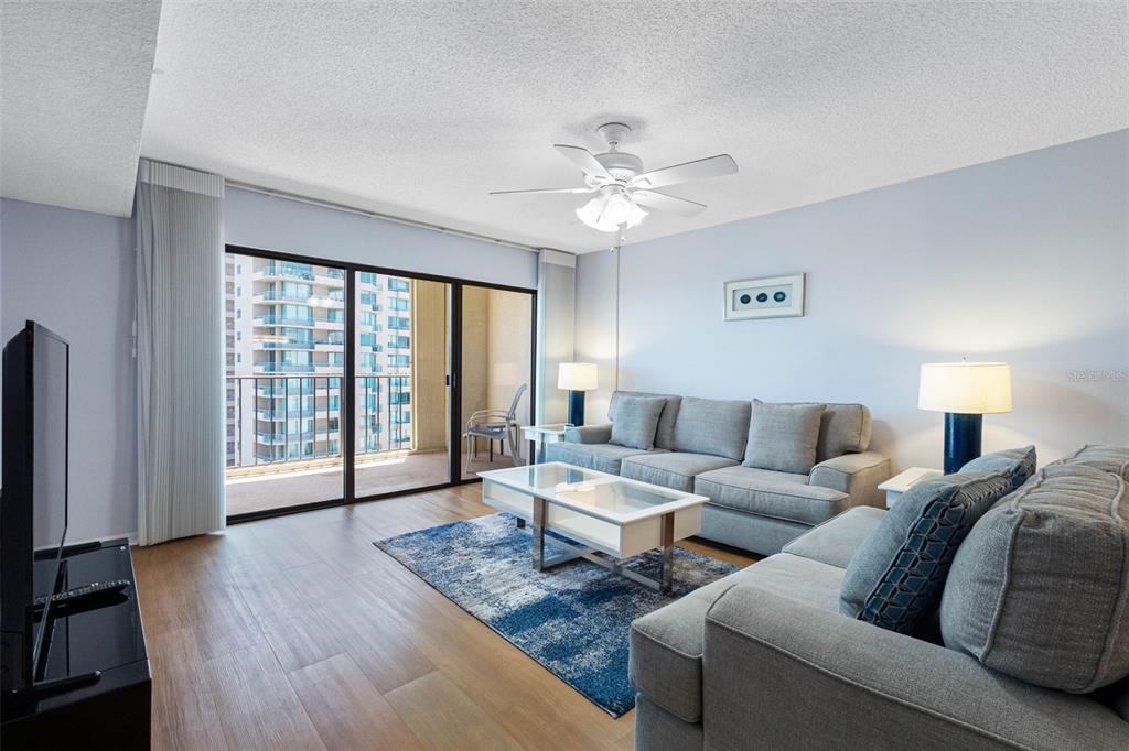 A living room features gray sofas, a blue area rug, and a balcony with city views — 1480 GULF BOULEVARD UNIT 1011, CLEARWATER BEACH, FL