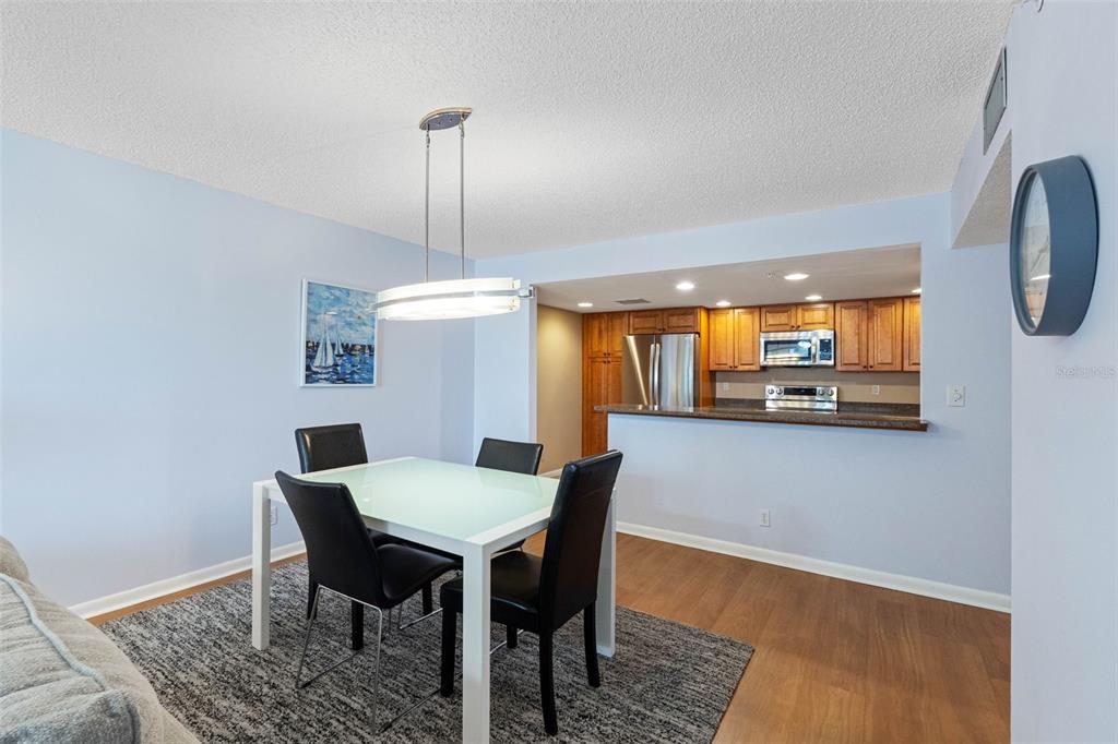 A dining area with a white table and black chairs sits before an open kitchen — 1480 GULF BOULEVARD UNIT 1011, CLEARWATER BEACH, FL