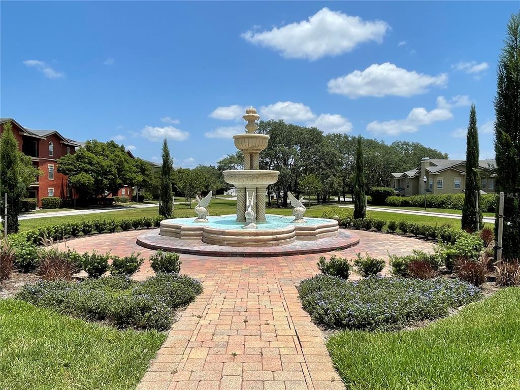 A stone fountain sits in the center of a brick courtyard surrounded by landscaped grounds — 102 VISTA VERDI CIRCLE UNIT 212, LAKE MARY, FL