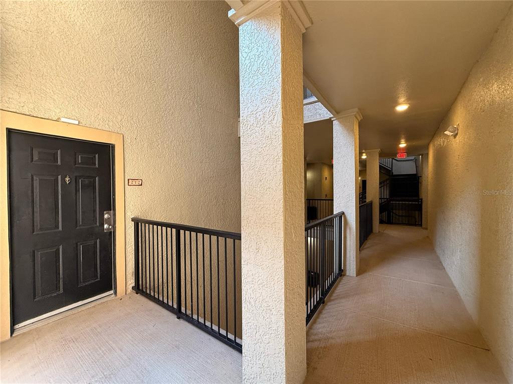 A black apartment door labeled 212 sits at the end of a covered outdoor hallway — 102 VISTA VERDI CIRCLE UNIT 212, LAKE MARY, FL