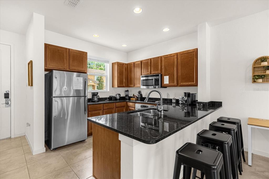 A kitchen features wooden cabinets, stainless steel appliances, a granite island, and black bar stools — 2634 CORVETTE LANE, KISSIMMEE, FL