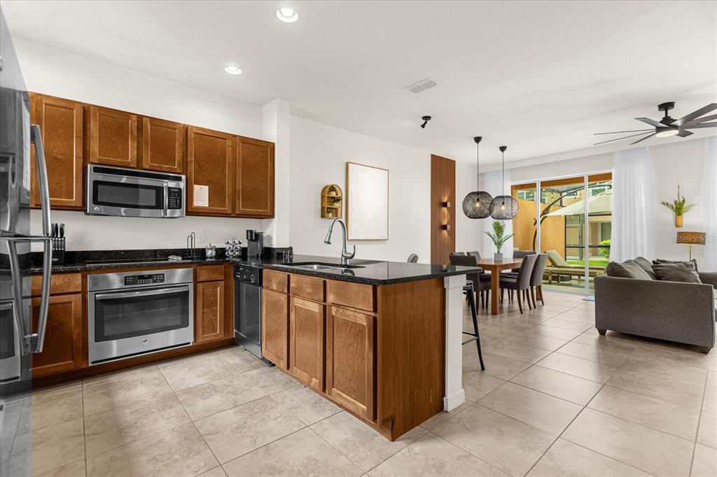 A kitchen with wood cabinets and granite countertops opens to a dining and living area — 2634 CORVETTE LANE, KISSIMMEE, FL