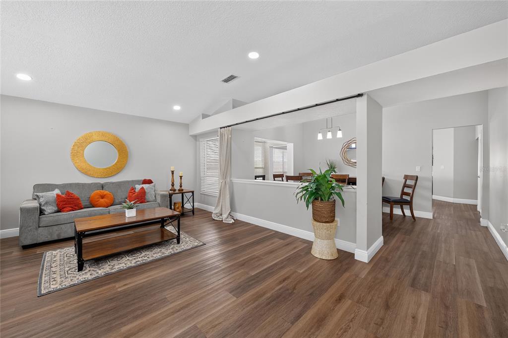 A living room with wood-look flooring, a gray sofa, and an open wall to the dining area — 8809 PARLIAMENT COURT, KISSIMMEE, FL